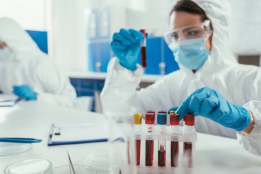 Biyokimyacı laboratuarda meslektaşının yanında kan örneğiyle birlikte test tüpü tutuyor.