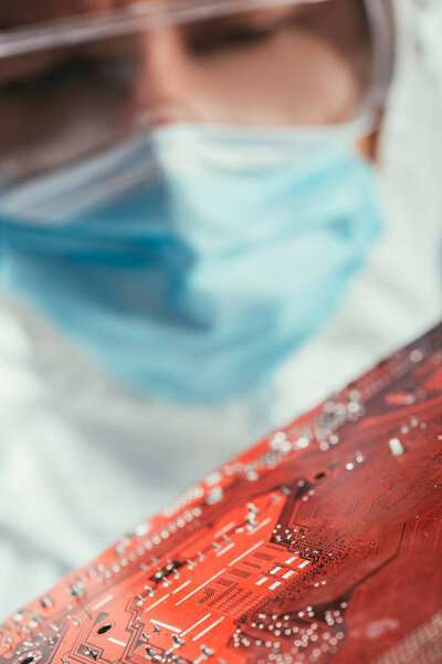 селективный фокус инженера в медицинской маске и очках с материнской платой компьютера
