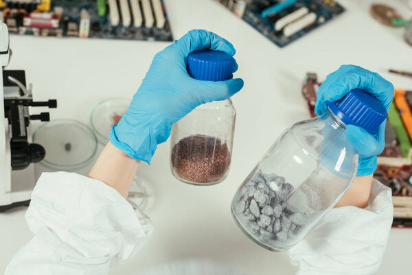 partial view of engineer holding jars with gravel near computer motherboards