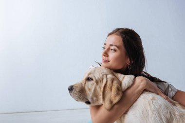 Çekici kız beyaz arka planda Golden Retriever 'a sarılırken başka tarafa bakıyor. 