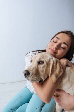 Çekici bir kadın, gözleri kapalı beyaz arka planda Golden Retriever 'ı kucaklıyor.