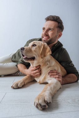 Gri arka planda Golden Retriever 'ı kucaklarken gülümseyen adamın seçici odağı