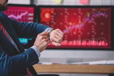 Veri analistinin kırpılmış görünümü masadaki bilgisayar monitörleri yanında kol saati ile zamanı kontrol ediyor 