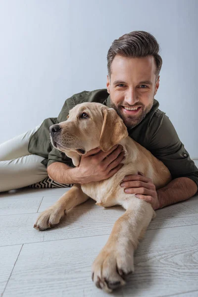 男人在灰色背景下在地板上爱抚金毛猎犬时对着相机微笑的选择性焦点 — 图库照片