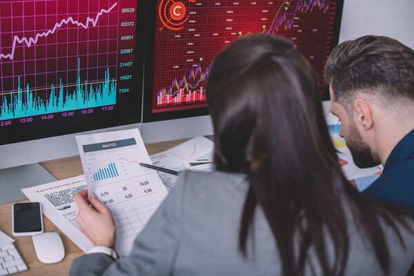 Selective focus of information security analysts planning work with charts on papers and computer monitors  