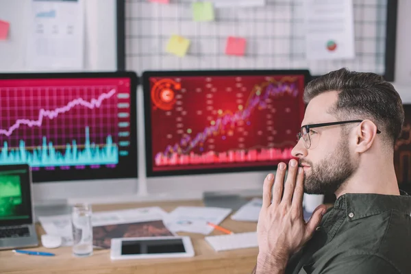 Side view of thoughtful computer system analyst looking away near digital devices on table