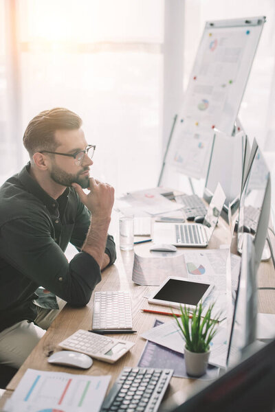 Side view of information security analyst working at table with digital devices and papers 