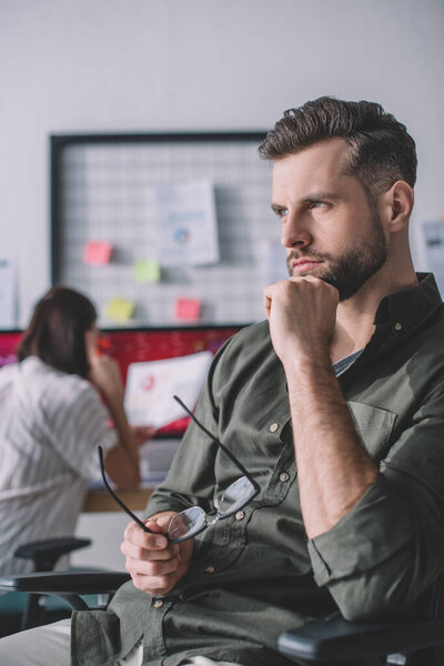 Selective focus of computer systems analyst looking away while colleague working in office 
