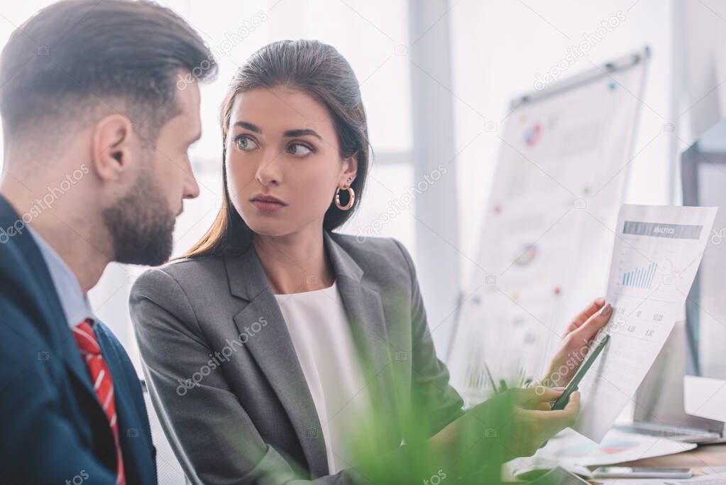 Selective focus of data analyst pointing on chart to colleague in office 