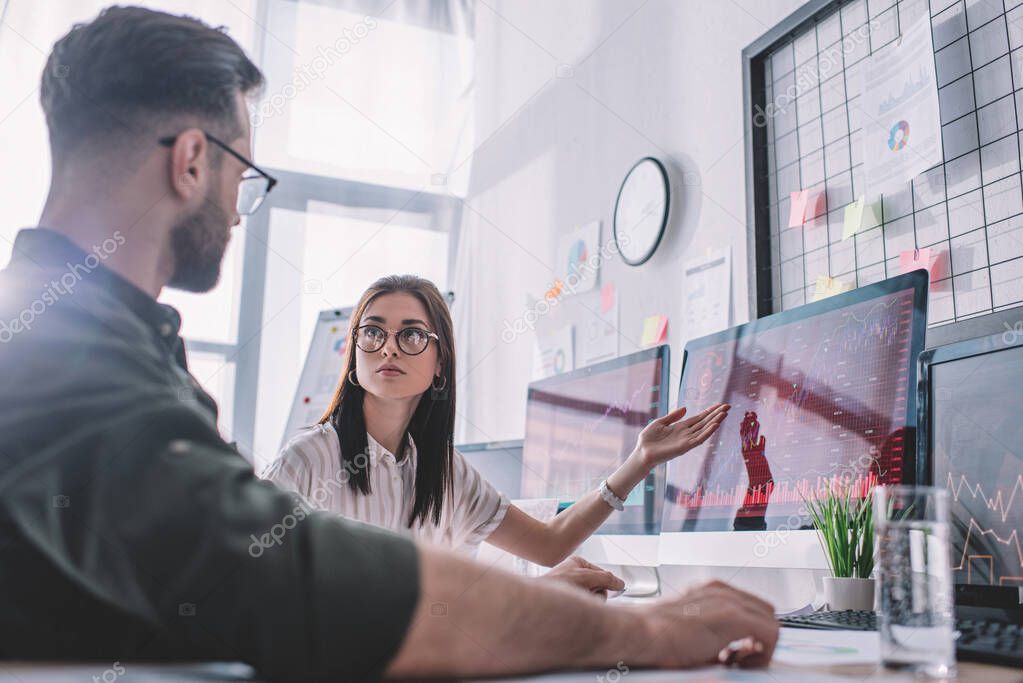 Selective focus of data analyst pointing with hand on computer monitor to colleague in office 