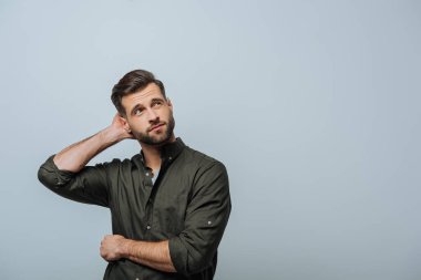 Pensive man with hand near head looking up isolated on grey clipart