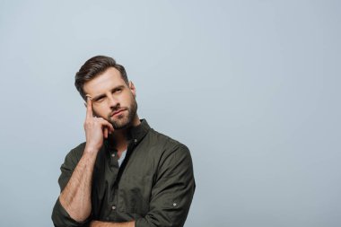 Dreamy man with finger near forehead looking away isolated on grey clipart