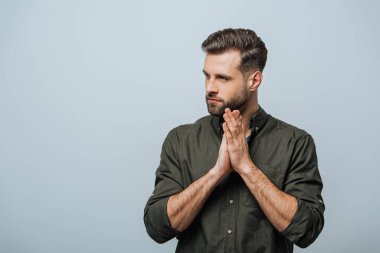 Handsome bearded man with praying hands looking away isolated on grey clipart