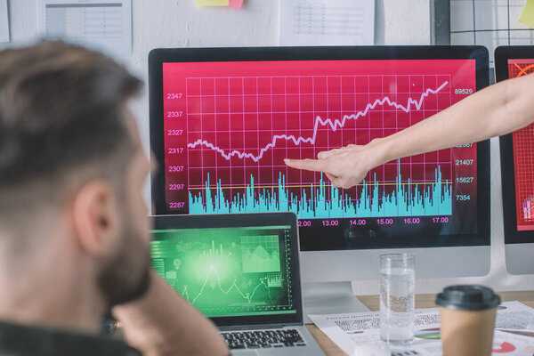 Selective focus of data analyst pointing at chart on computer monitor to colleague in office 