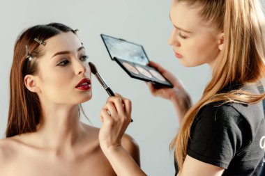 Güzel makyaj sanatçısı beyaz üzerine izole edilmiş çekici bir modele kapatıcı sürüyor. 