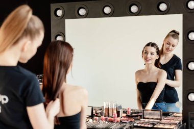 Makyaj sanatçısının dekoratif kozmetik ürünlerinin yakınında çekici bir modelin saçına dokunmasının seçici odağı 