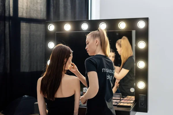 穿着黑色T恤的女人 化妆艺术家用字体在模特身上装饰化妆品 — 图库照片