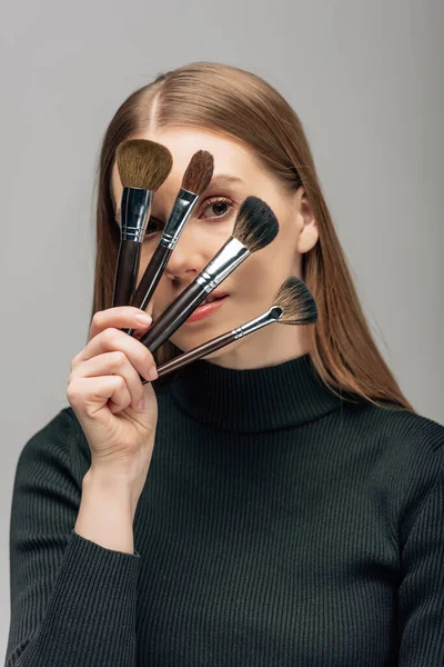 Joven Artista Maquillaje Cubriendo Cara Con Cepillos Cosméticos Aislados Gris — Foto de Stock