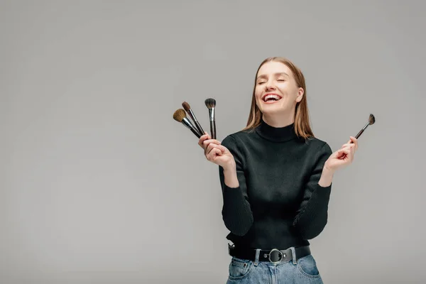 Happy makeup artist holding makeup brush set isolated on grey — Stock Image Happy Makeup Artist Holding Makeup Brush Set Isolated Grey Stock Photo