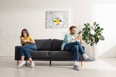 Genç çift evdeki koltukta akıllı telefon kullanıyor. 
