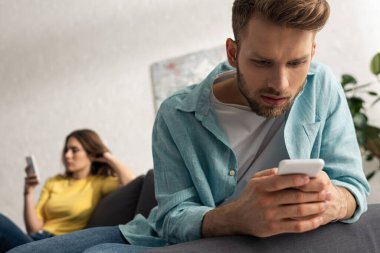 Kanepede kız arkadaşının yanında akıllı telefon kullanan bağımlı bir adamın seçici odağı. 