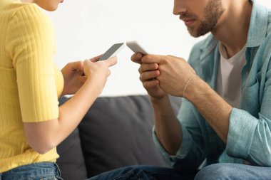 Kanepede otururken akıllı telefonlarla sohbet eden genç çiftin görüntüsü. 