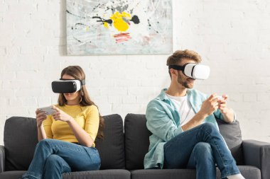 VR kulaklıklı genç çift koltukta akıllı telefon kullanıyor. 