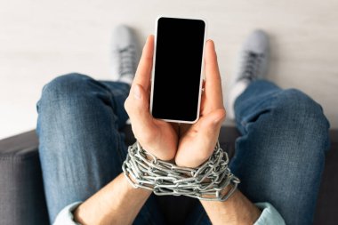 Zincirli, akıllı telefonu olan, elleri bağlı bir adam. 