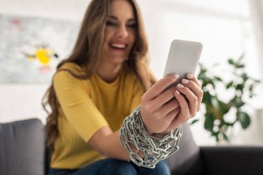 Akıllı telefon kullanan, elleri zincirli, gülümseyen bir kadının seçici odağı 