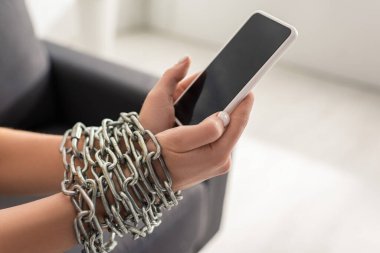 Ellerinde metal zincir olan, elinde boş ekranlı akıllı telefon tutan bir kadının görüntüsü. 