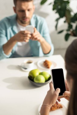 Seçici odak noktası, erkek arkadaşıyla kahvaltı ederken beyaz ekranlı akıllı telefon kullanması. 