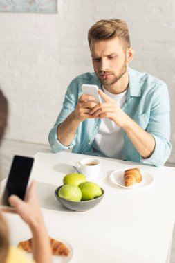 Erkeğin mutfakta kahvaltıda kız arkadaşının yanında akıllı telefon kullandığı seçmeli bir odak noktası. 