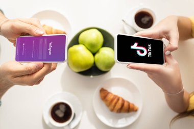 KYIV, UKRAINE - 21 Şubat 2020: Instagram ve TikTok uygulamalarıyla kahvaltı masasına yakın akıllı telefon kullanan çiftin üst görünümü 