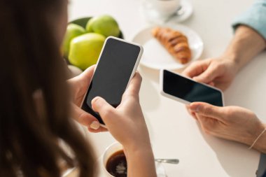 Seçici odak noktası, mutfakta kahvaltı yaparken erkek arkadaşının yanında akıllı telefon tutan kadın. 