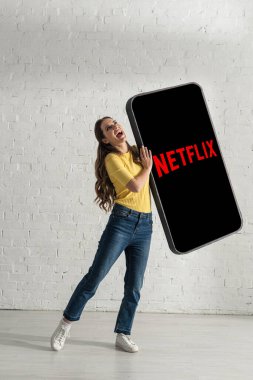 KYIV, UKRAINE - 21 Şubat 2020: Evde netflix uygulamalı akıllı telefon modelini tutarken gülen çekici kadın 