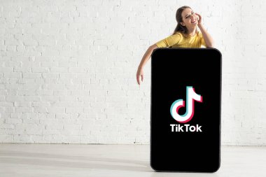 KYIV, UKRAINE - 21 Şubat 2020: Akıllı telefon modelinde TikTok uygulamasının yakınındaki kameraya bakan olumlu kadın 