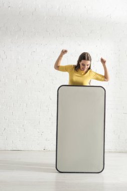 Güzel bir kadın gülümsüyor ve evdeki akıllı telefonun büyük bir modelinin yanında jest yapıyor. 