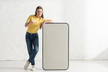 Gülümseyen kadın akıllı telefon modelini işaret ediyor. 