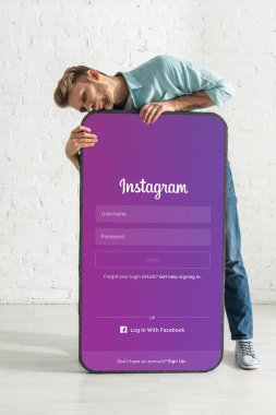 KYIV, UKRAINE - 21 Şubat 2020: Instagram uygulaması ile akıllı telefonun büyük modelini öpen yakışıklı adam 