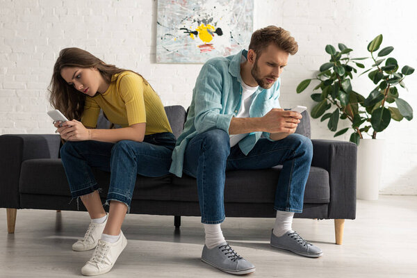 Depended couple using smartphones on couch in living room