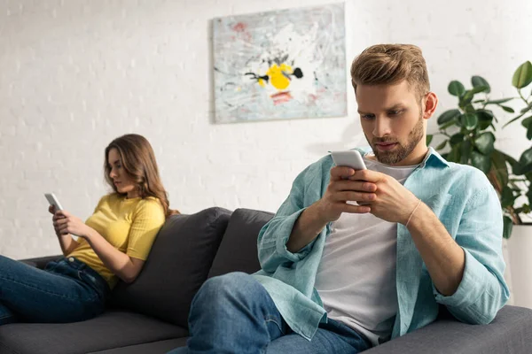 Kanepede kız arkadaşının yanında akıllı telefon kullanan bir adamın seçici odağı. 