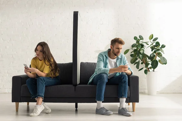 年轻夫妇在客厅用智能手机在沙发上使用智能手机的模型 — 图库照片