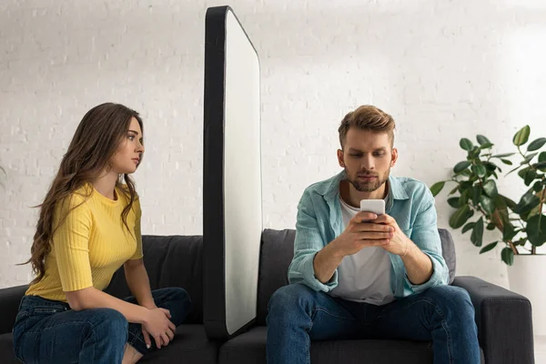 一个英俊的男人在智能手机大模特和沙发上的女朋友身边聊天 — 图库照片