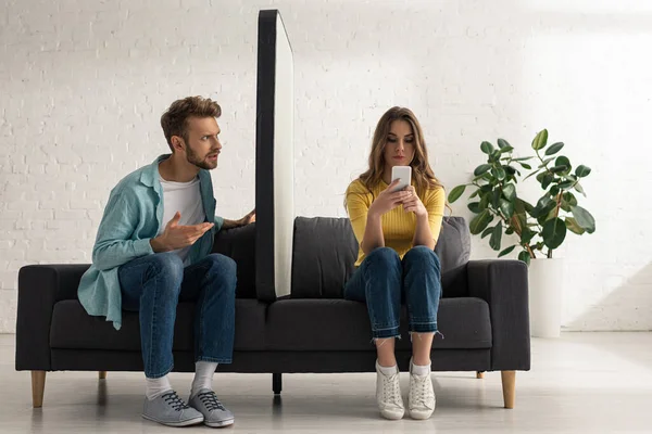 Confused Man Looking Girlfriend Chatting Big Model Smartphone Sofa — Stock Photo, Image