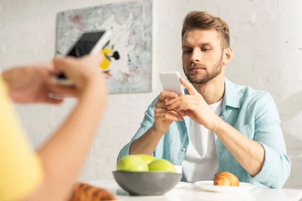 男人在厨房吃早餐时用智能手机接近女朋友的选择性焦点 — 图库照片