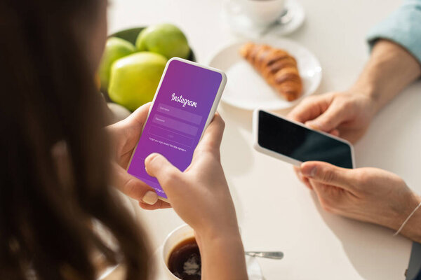 КИЕВ, УКРАИНА - 21 ФЕВРАЛЯ 2020: Выборочный фокус женщины, использующей смартфон с приложением Instagram возле бойфренда во время завтрака на кухне
 