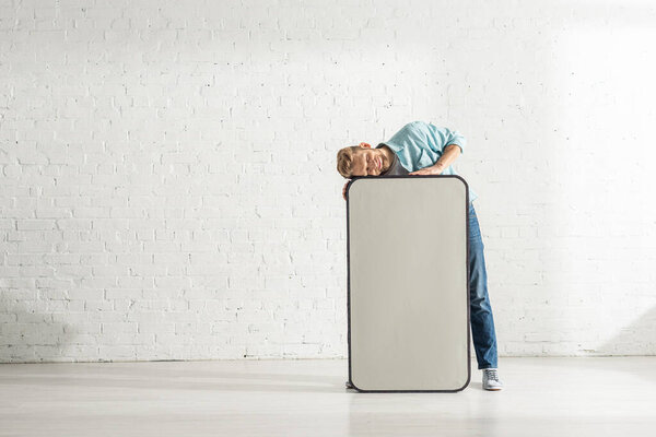 Улыбающийся мужчина стоит рядом с огромной моделью смартфона возле белой кирпичной стены
 