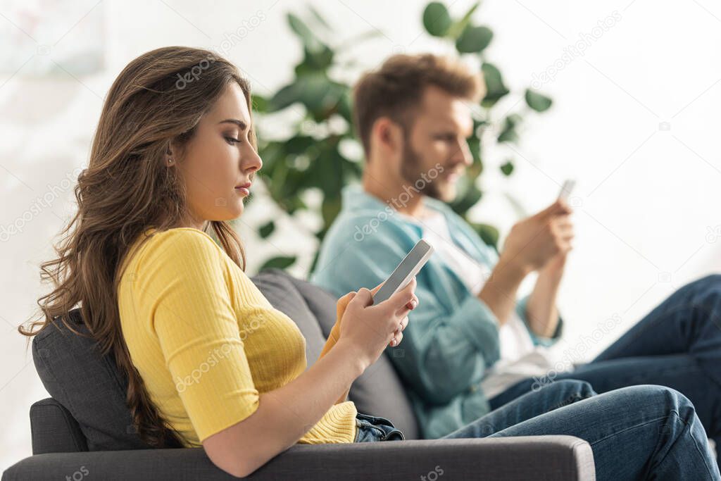 Side view of young woman using smartphone with blank screen near boyfriend on couch 