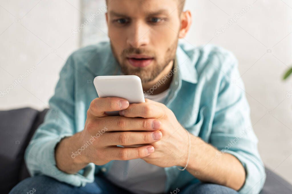 Selective focus of addicted man using smartphone on couch 