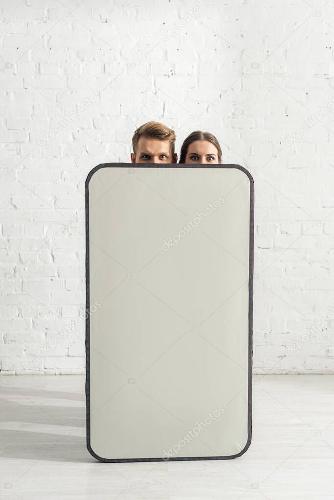 Young couple looking at camera near big model of smartphone at home 